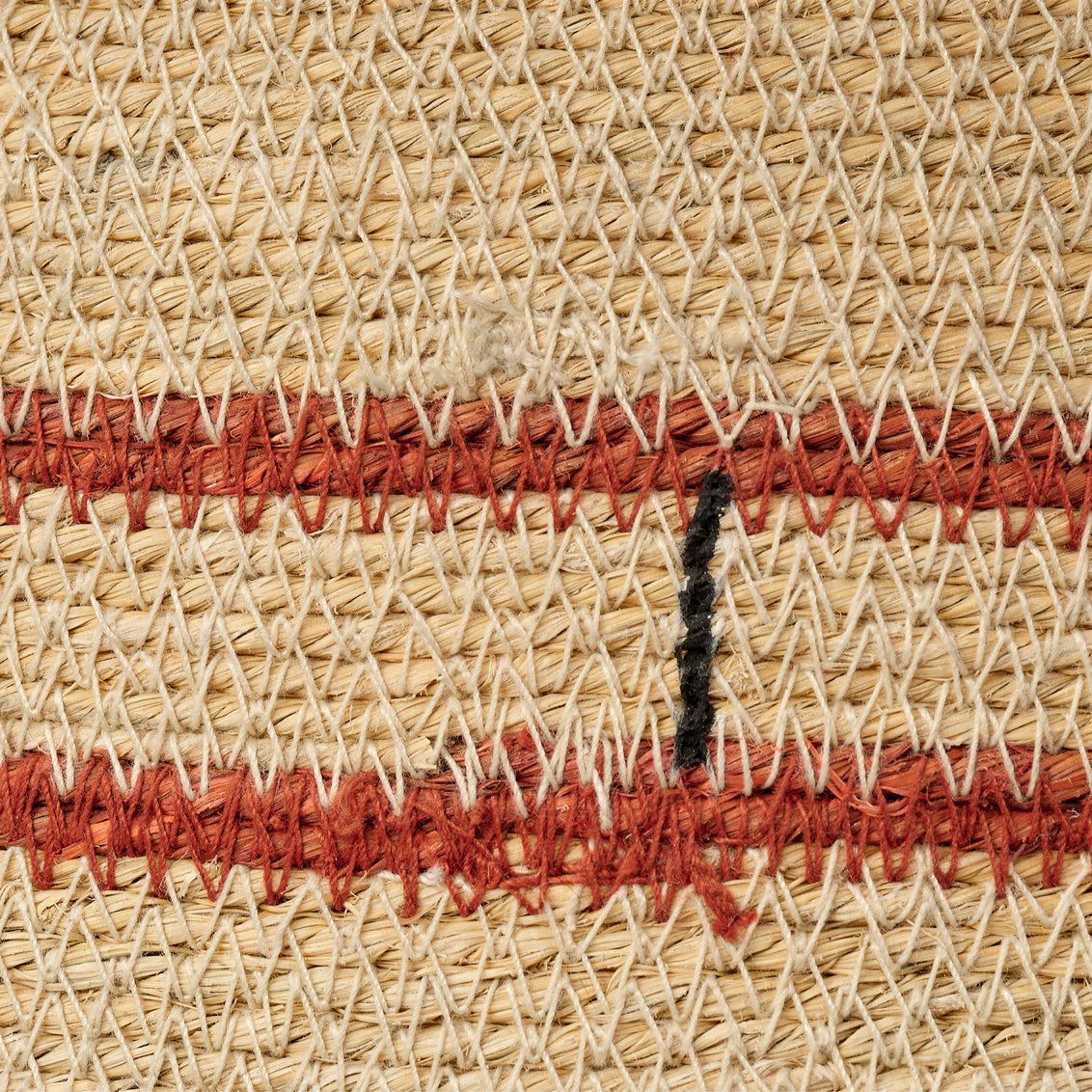Close-up of woven straw with red and black stitching