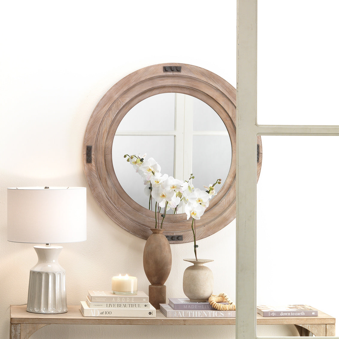 Round wooden mirror on a wall with decorative items on a table below.