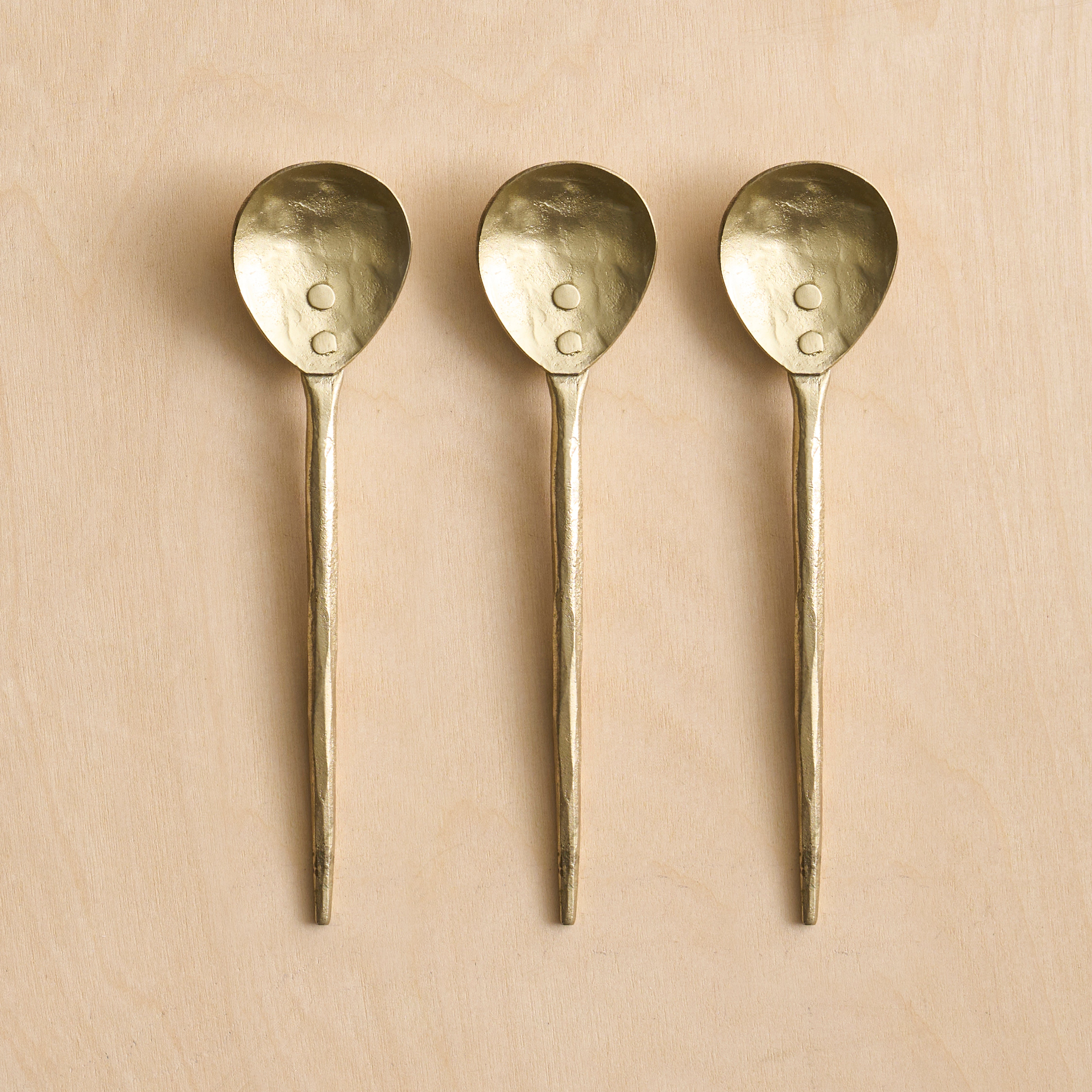 Three brass spoons with textured handles on a beige background