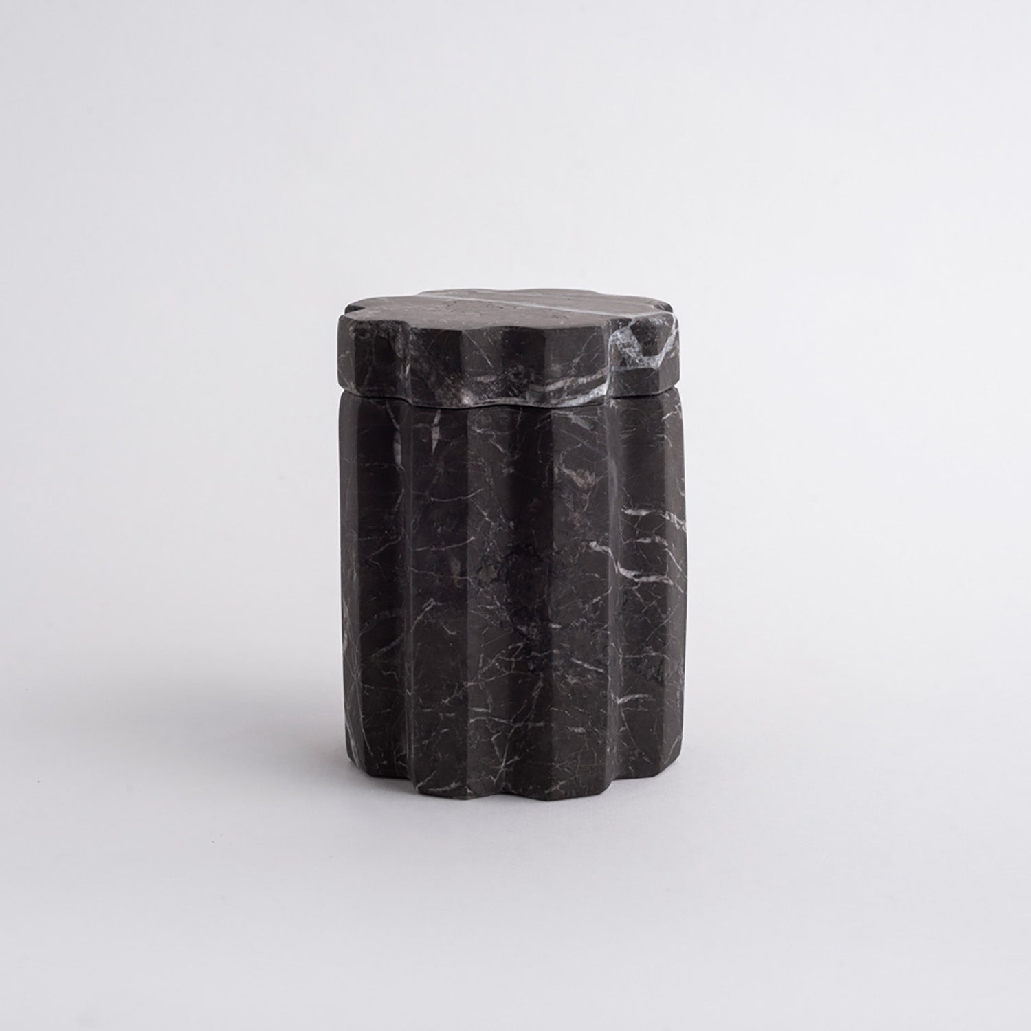 Black marble cylindrical container with a lid on a light gray background