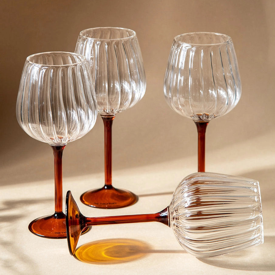 Set of four clear wine glasses with brown stems on a beige background