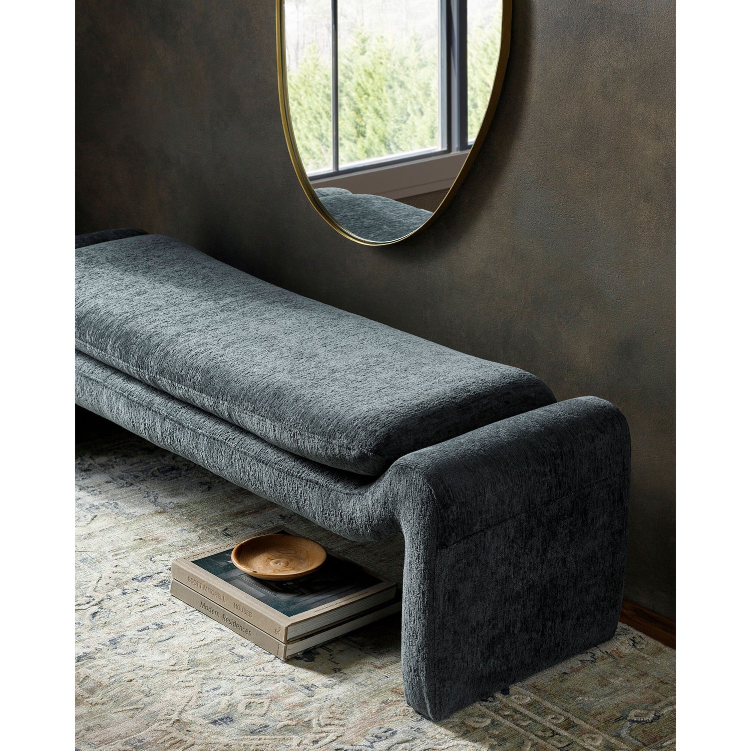 Gray upholstered bench in a room with a round mirror on the wall.