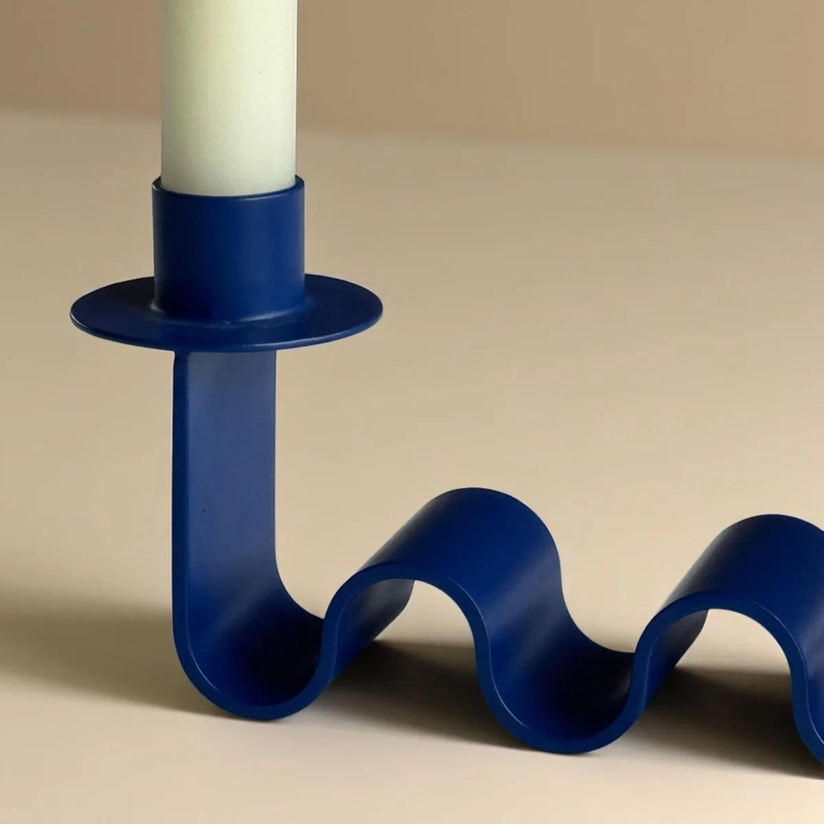 Blue wavy candle holder with a white candle on a beige background