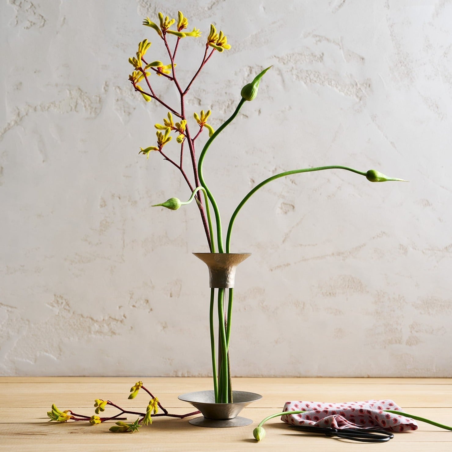 Vase with yellow flowers on a wooden surface against a beige wall