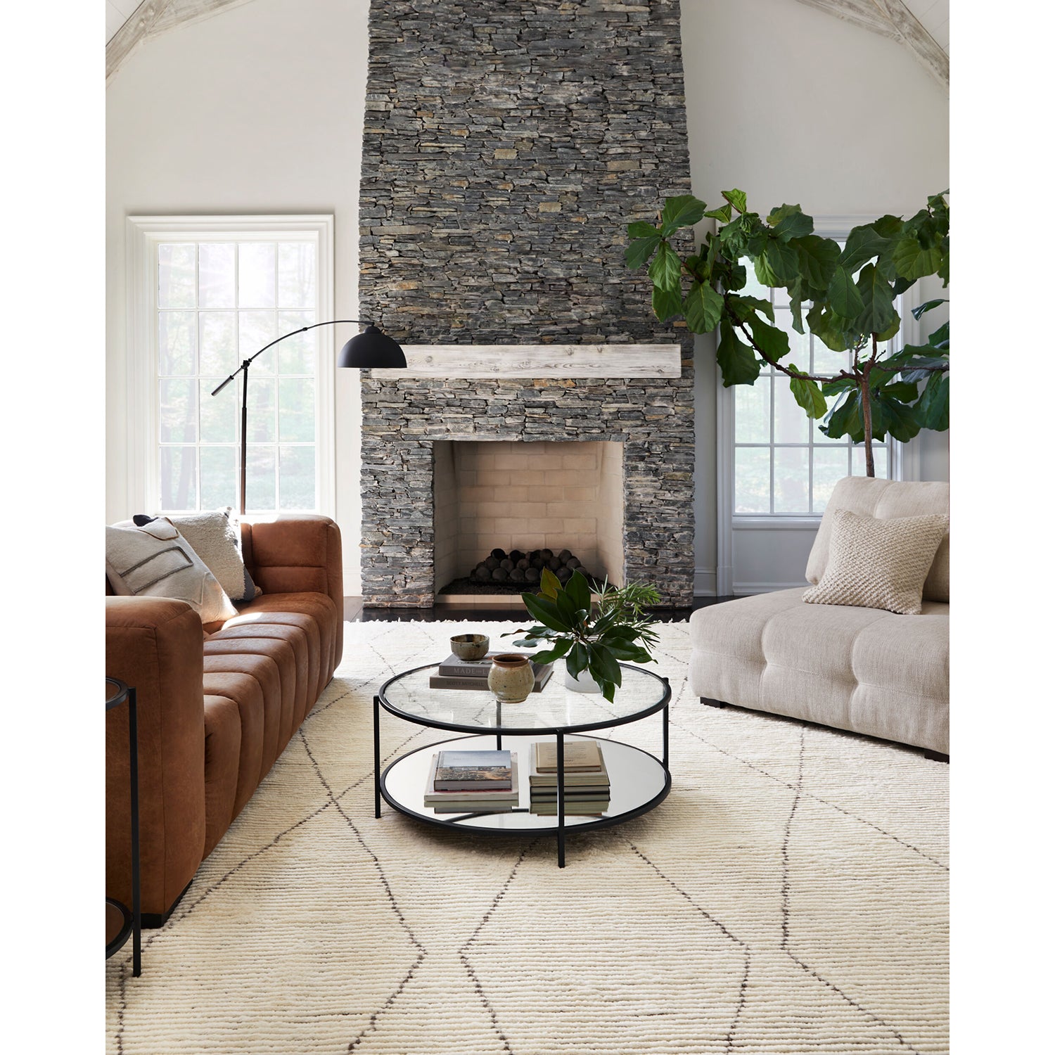 Modern living room with a stone fireplace, brown leather sofa, and white armchair.