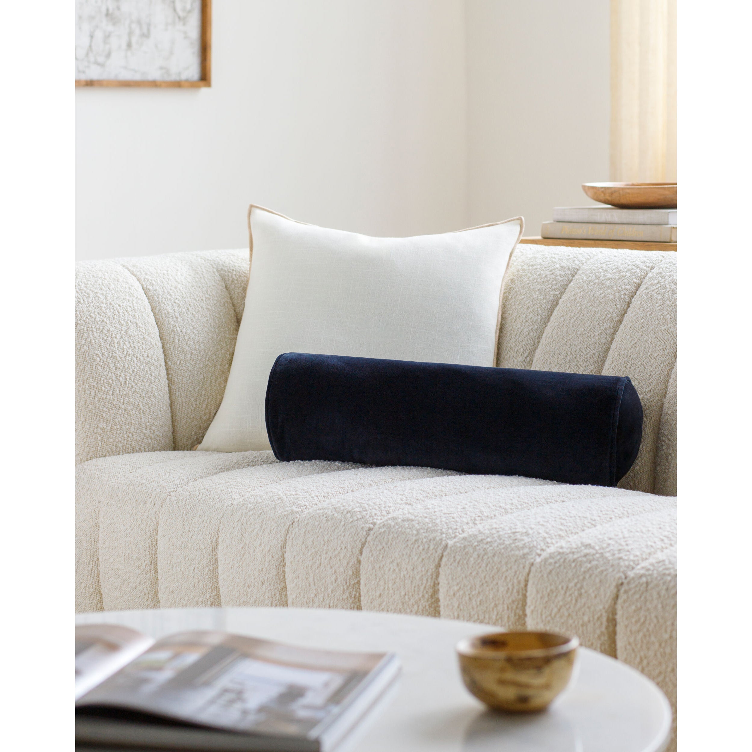 White pillow and navy bolster on a beige sofa with a coffee table in the foreground