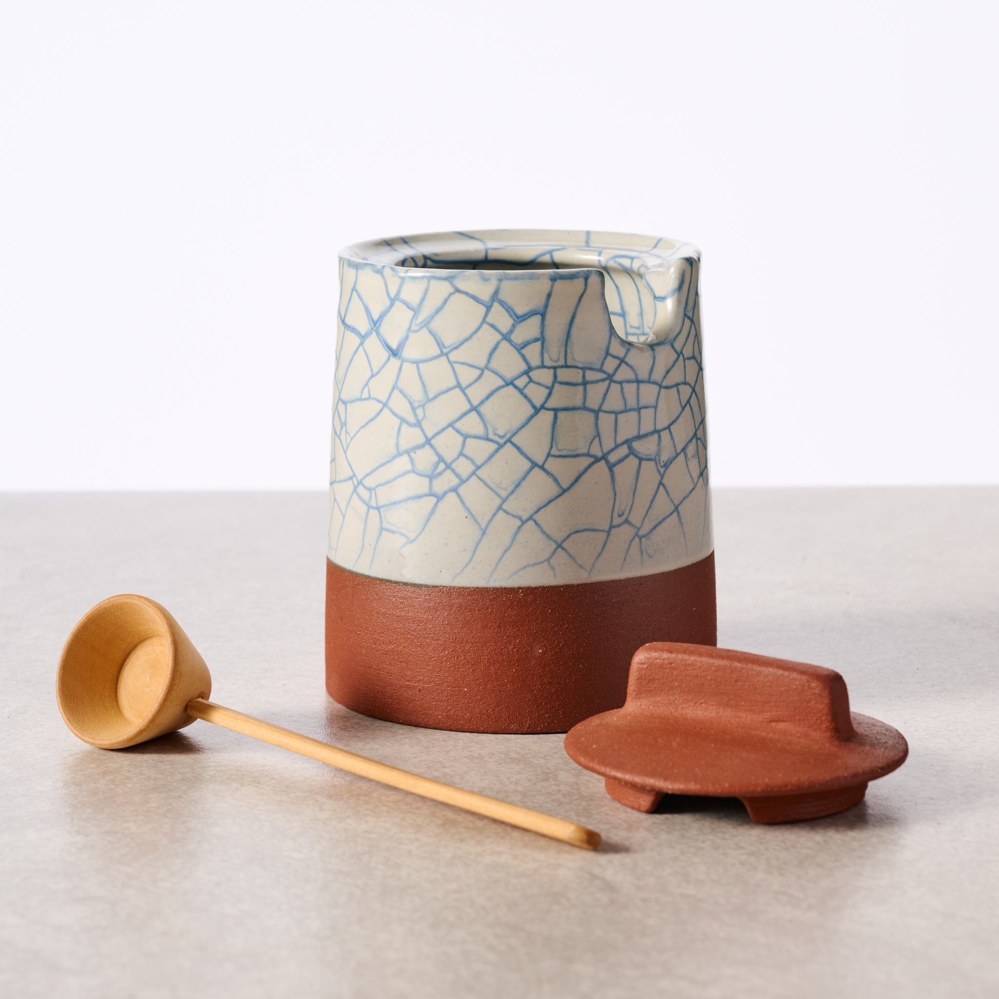 Ceramic container with crackle glaze, wooden scoop, and lid on a light surface.
