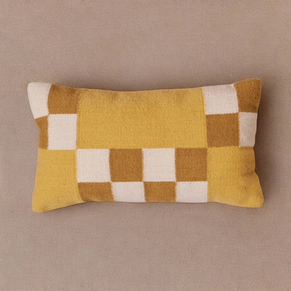Checkered pillow with yellow, brown, and white pattern on a beige background