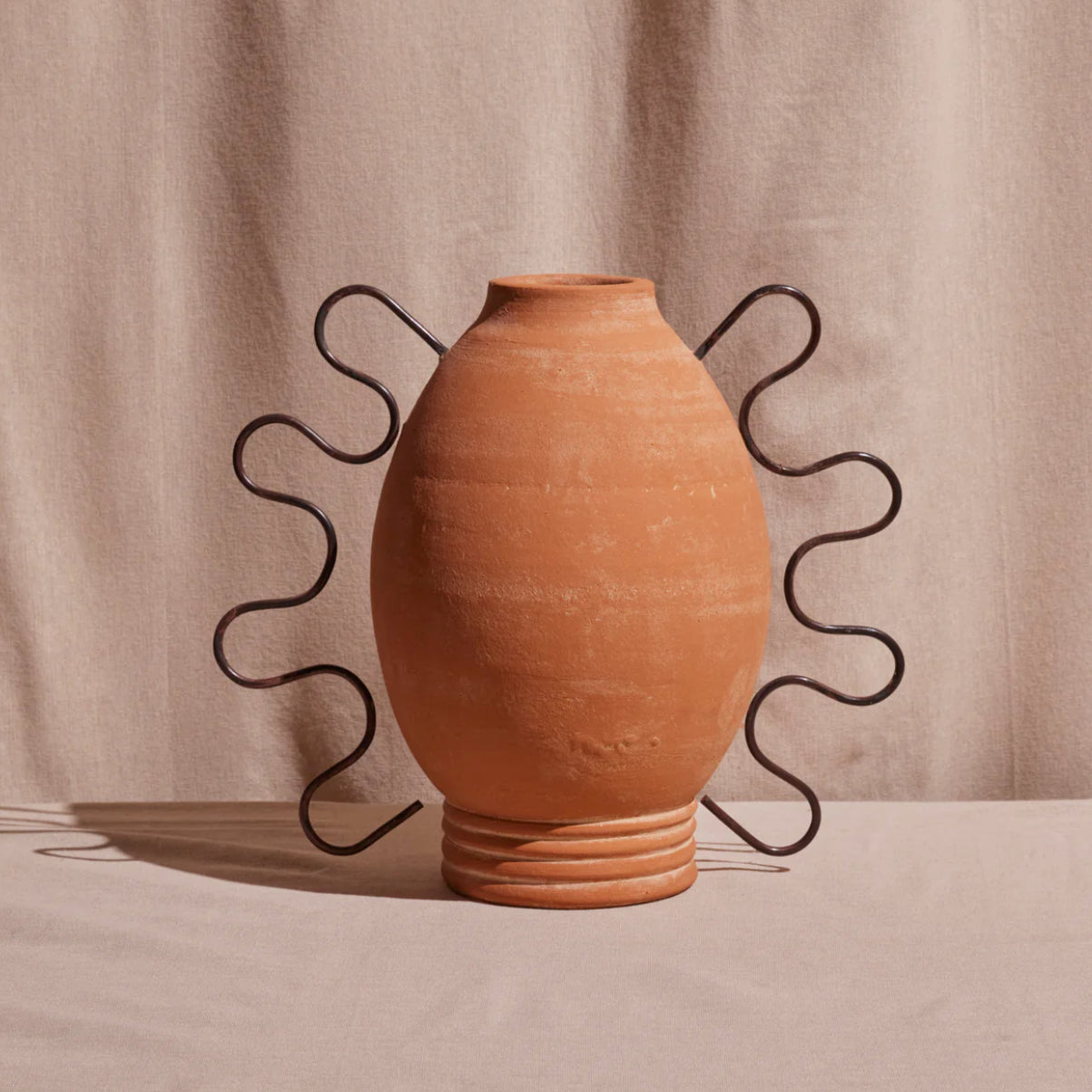 Terracotta vase with wavy metal stand on a beige background