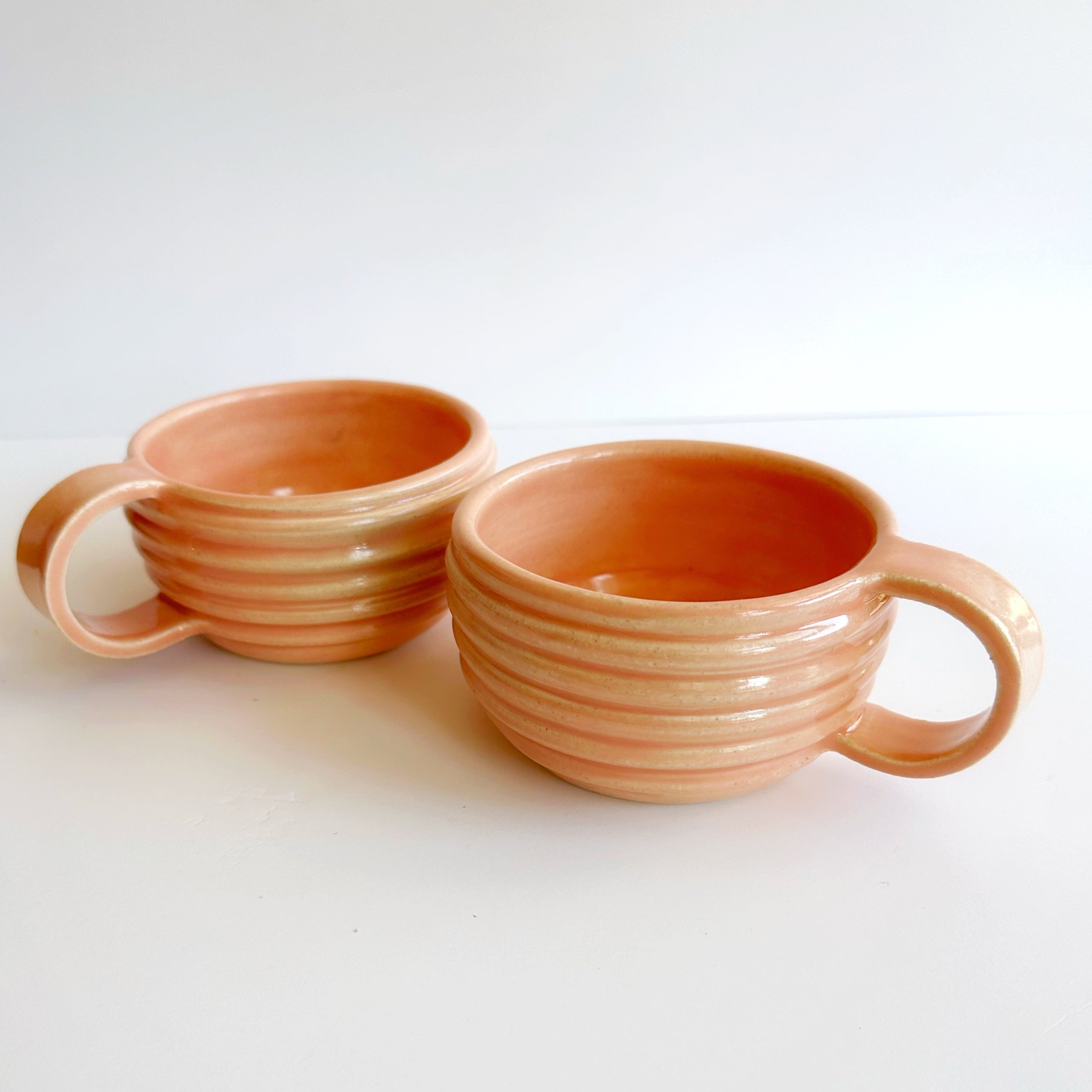Two terracotta-colored ceramic mugs with handles on a white background
