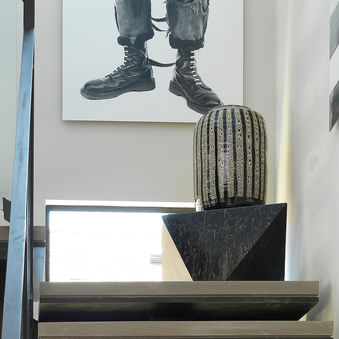 Decorative vase on a shelf with a painting of boots in the background