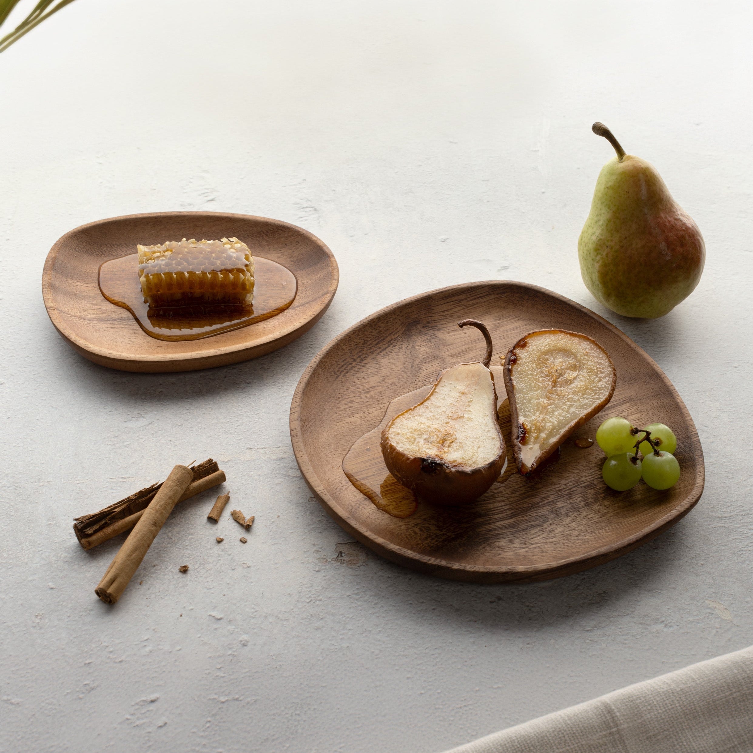 Wooden plates with sliced pears, honey, and grapes on a light surface.