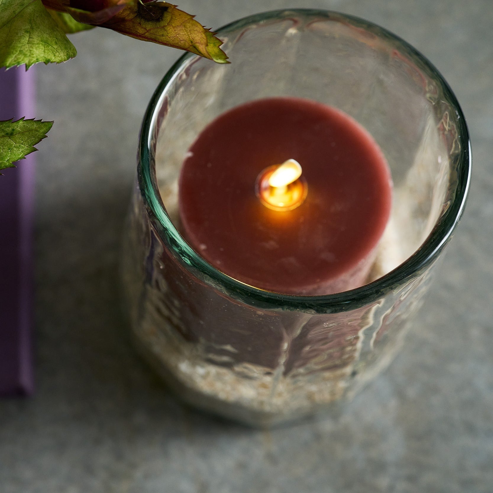 Candle in a glass holder with leaves on a gray surface