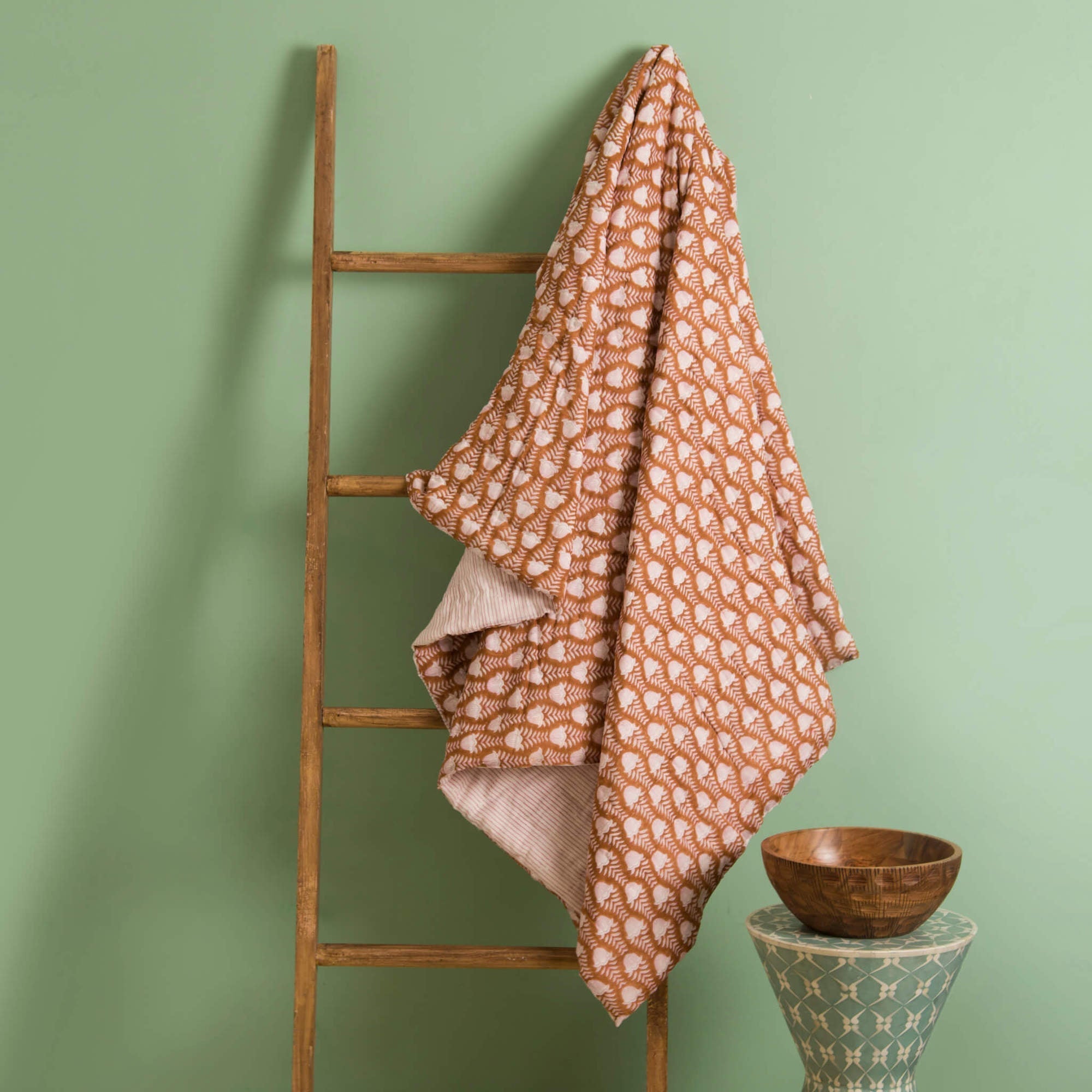 Orange patterned blanket draped over a wooden ladder against a green wall.