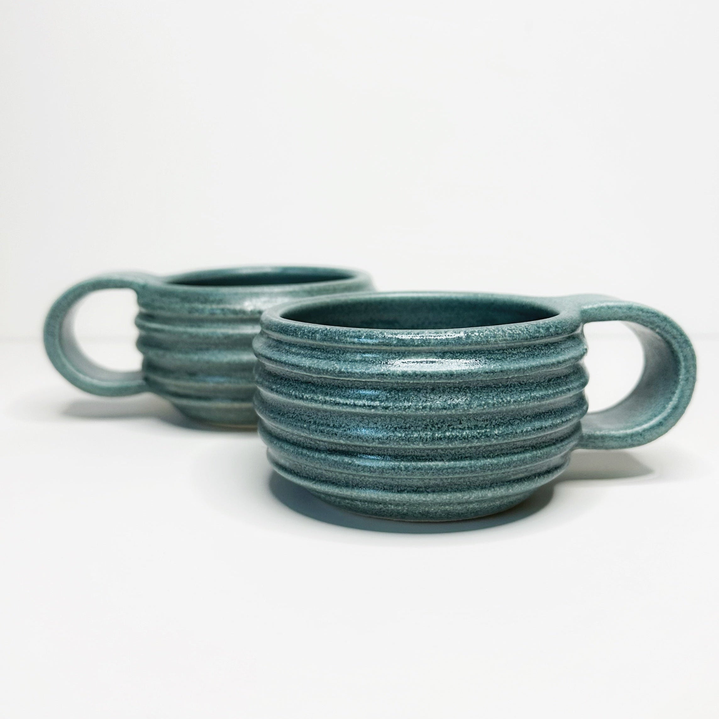 Two teal ceramic mugs with handles on a white background
