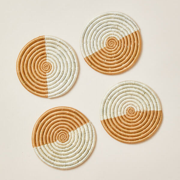 Four round woven coasters with a two-tone design on a beige background