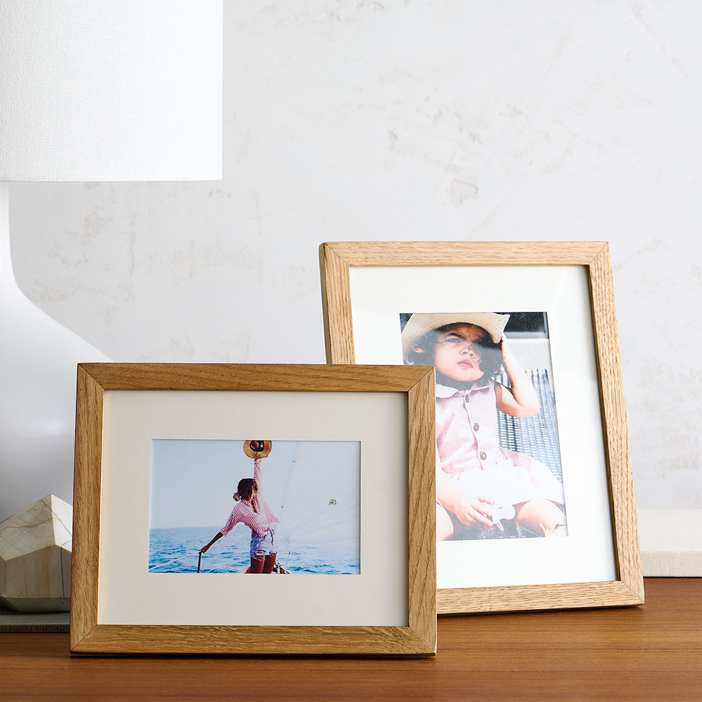 Two wooden picture frames with photos of people on a table against a white wall.