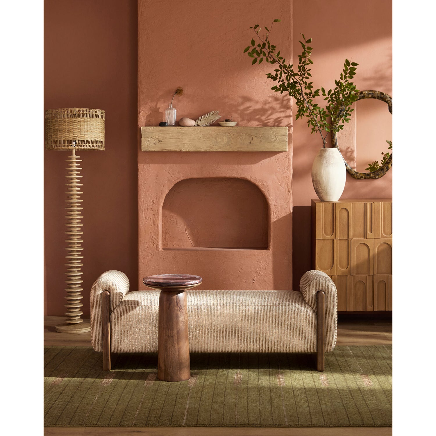 Cozy living room with a beige armchair, wooden side table, and decorative lamp against a pink wall.