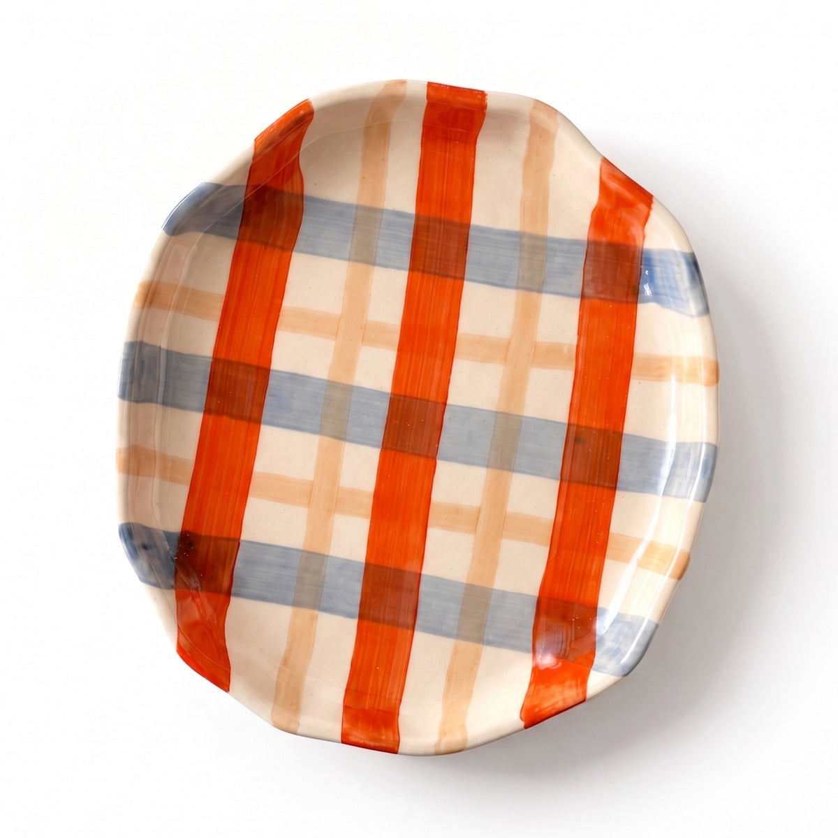 A scalloped ceramic plate with a plaid pattern featuring bold orange stripes, light blue-gray stripes, and thin beige stripes on a white background.