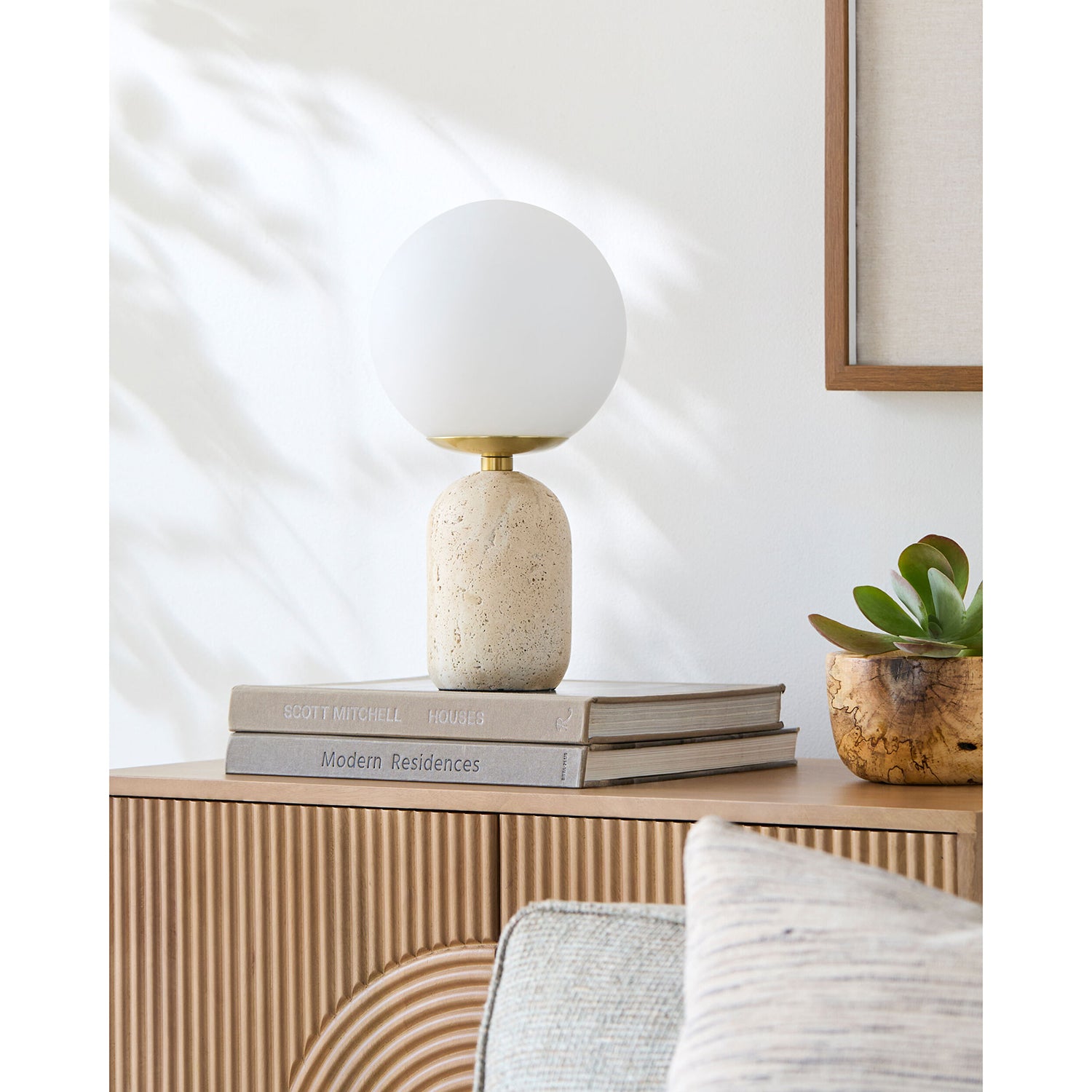 Decorative lamp on a wooden side table with books and a plant in a minimalistic room.
