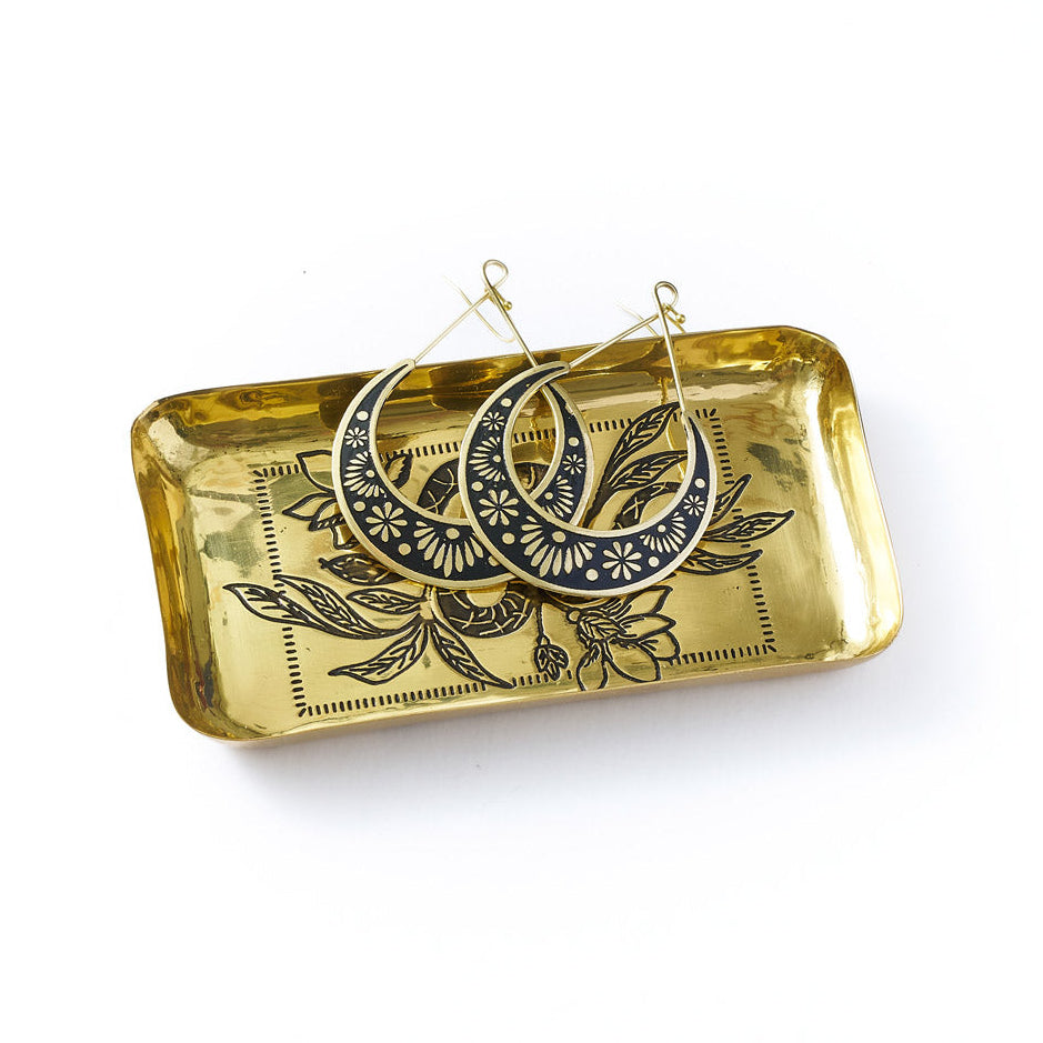 Brass tray with decorative earrings on a white background