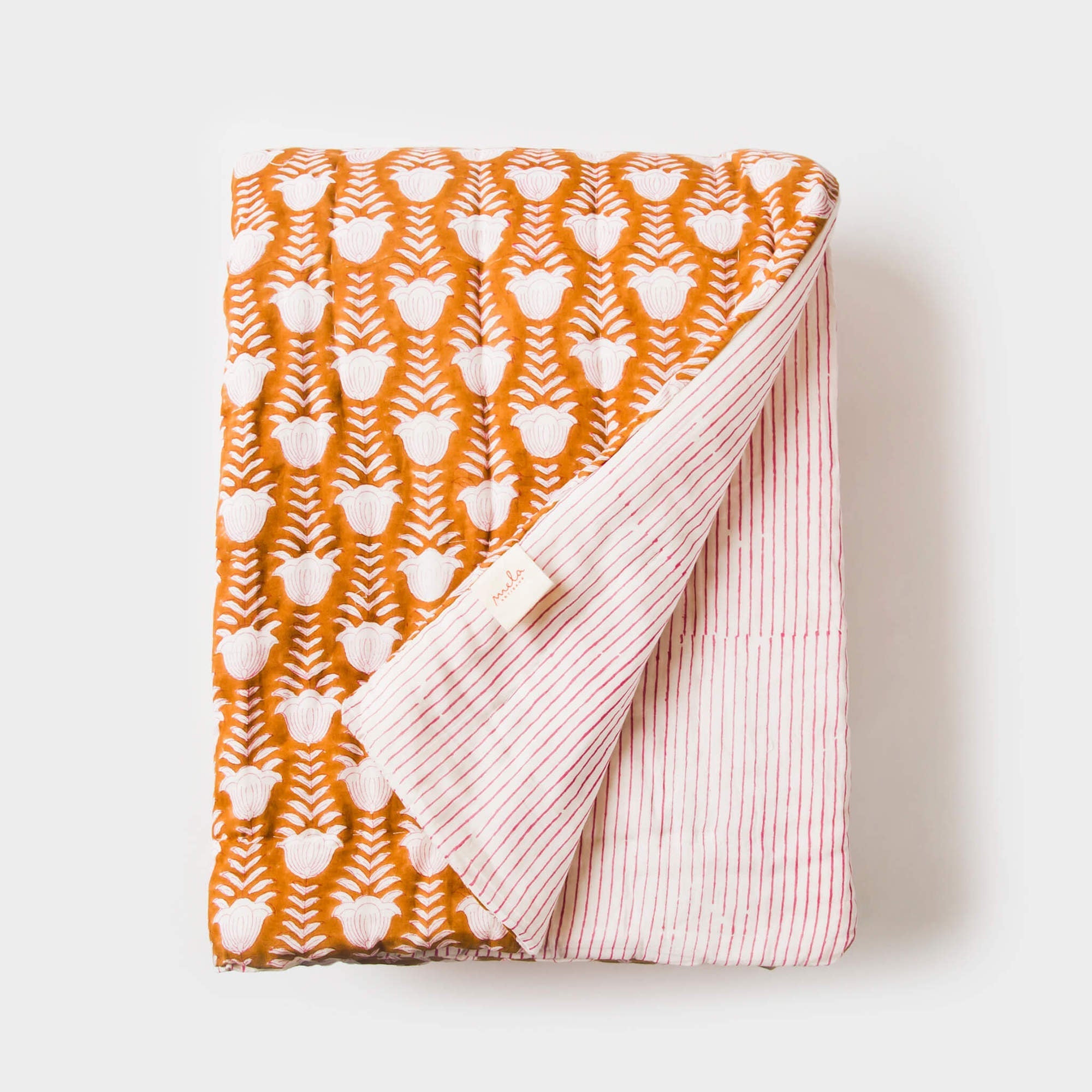 Folded blanket with orange and white tulip pattern on one side and pink and white striped pattern on the other, on a light background.