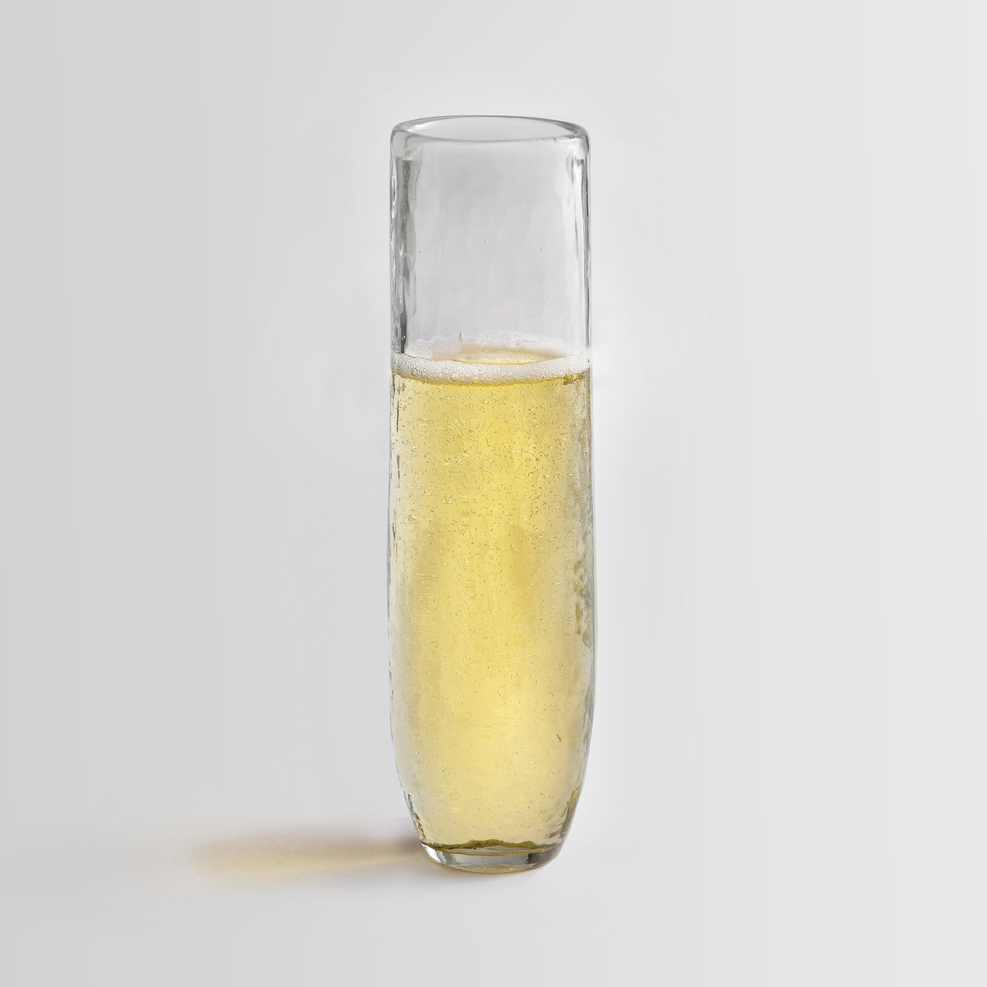 Clear flute glass filled with a yellowish liquid on a light gray background