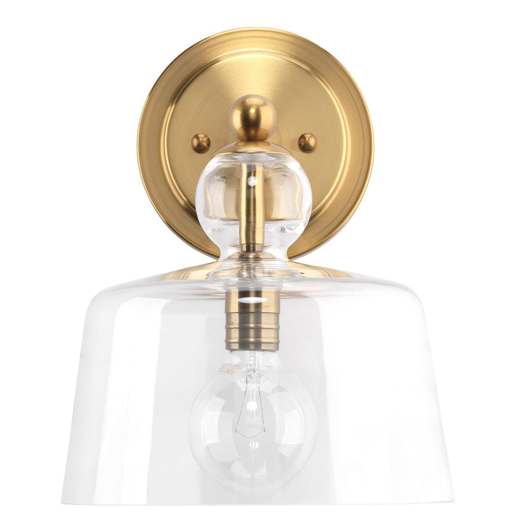 Wall-mounted light fixture with gold finish and clear glass shade on a white background
