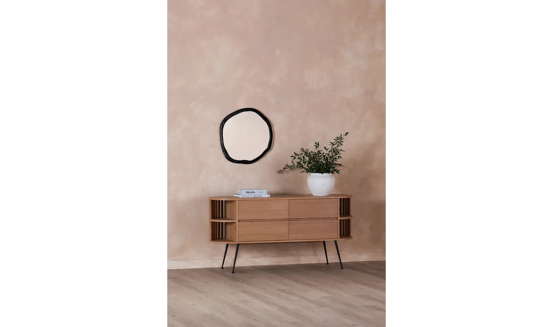 Wooden sideboard against a beige wall with a round mirror and plant on top