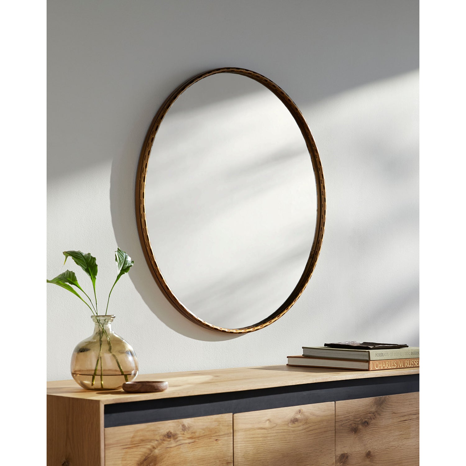 Round gold mirror with wooden frame on a wall above a wooden console table.