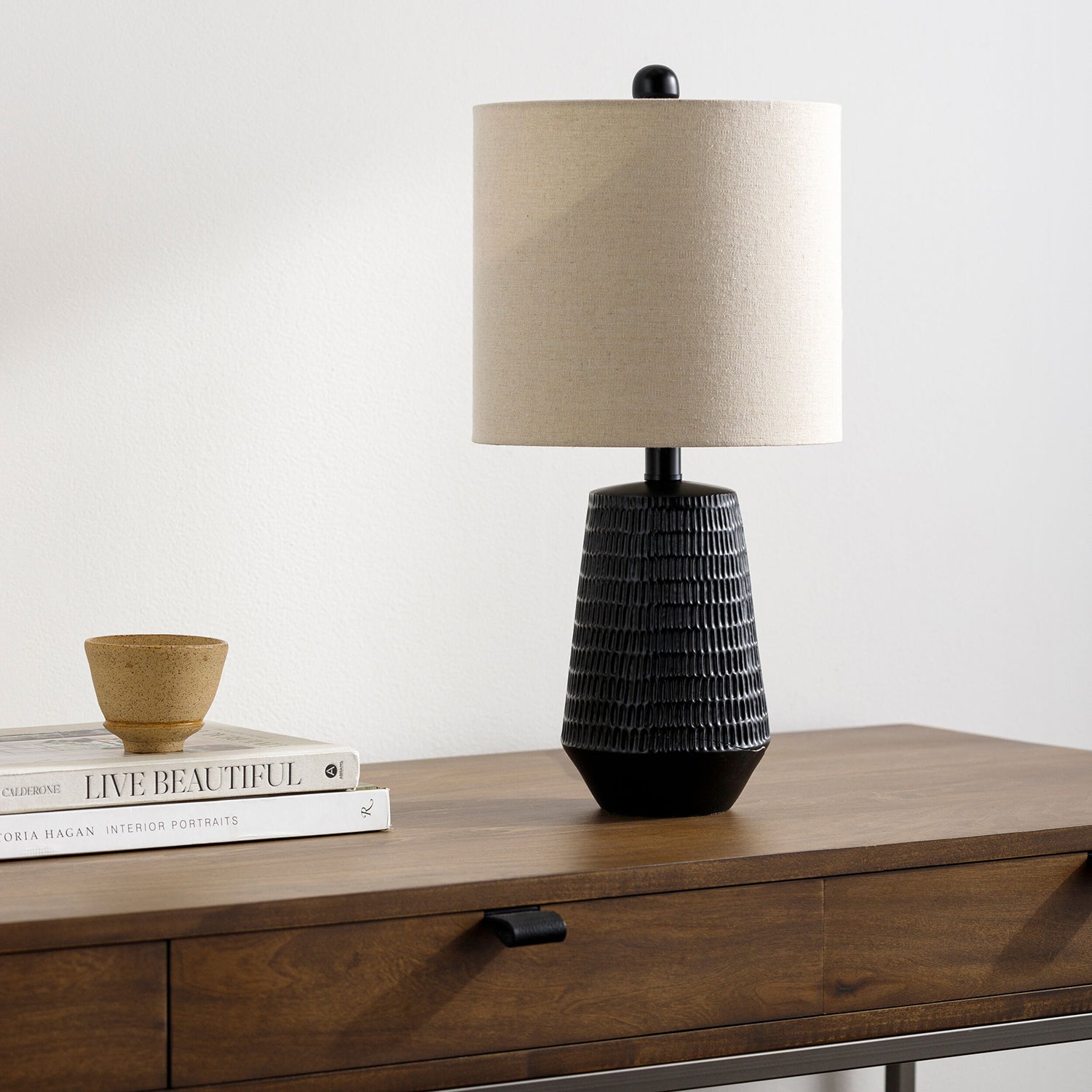 Table lamp with a textured black base and beige shade on a wooden surface.