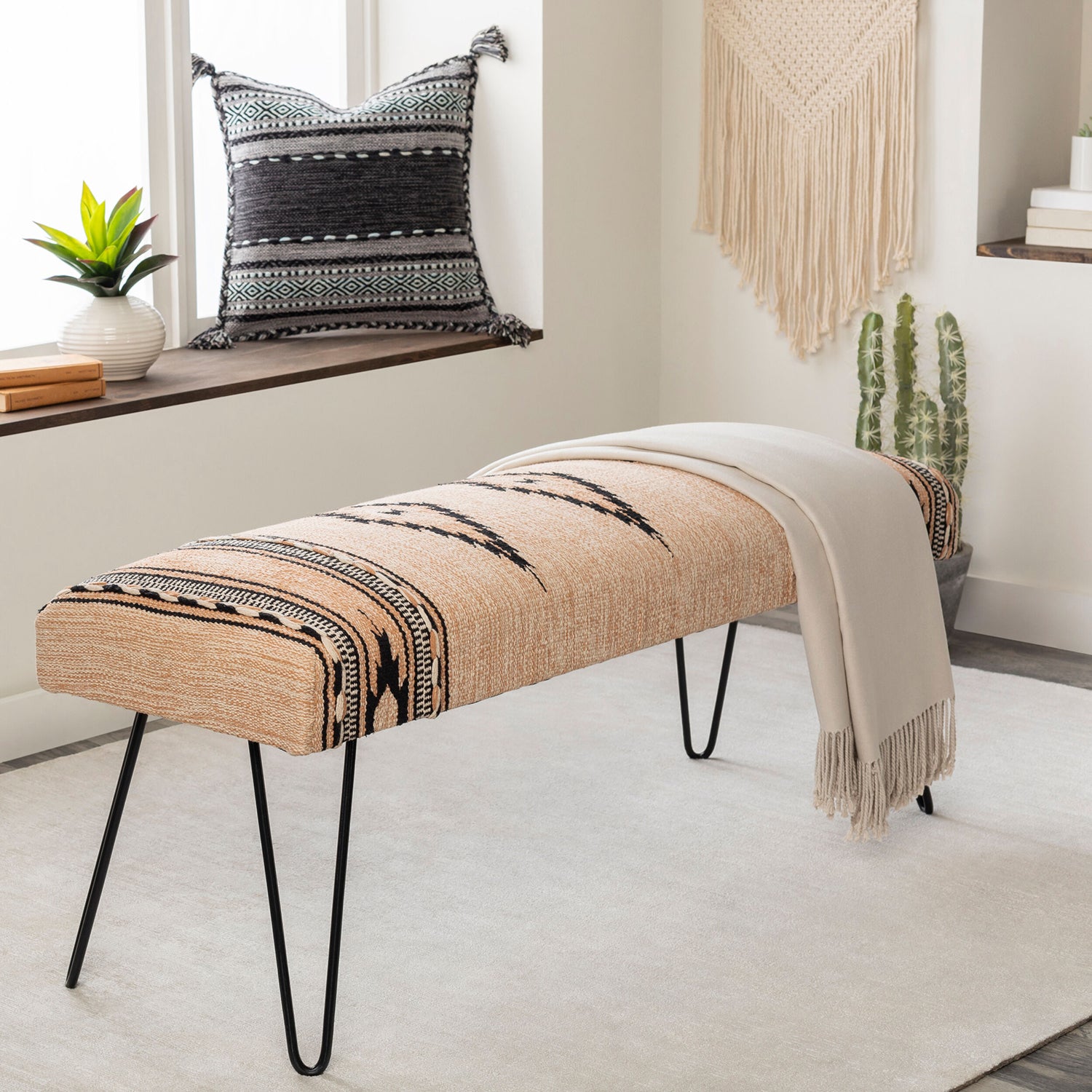 Beige bench with black patterned cover in a room with a window, plant, and decorative items.