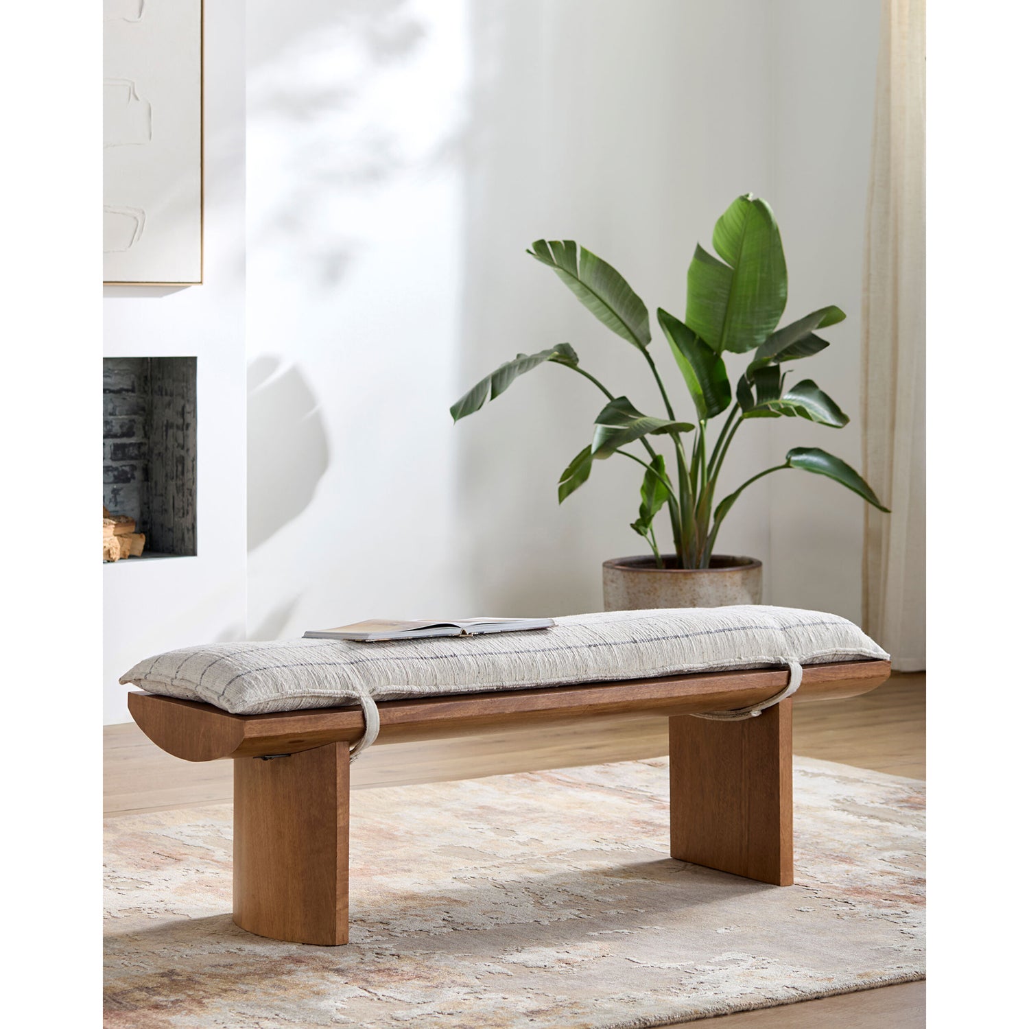 Wooden bench with a cushion in a room with a plant and fireplace.