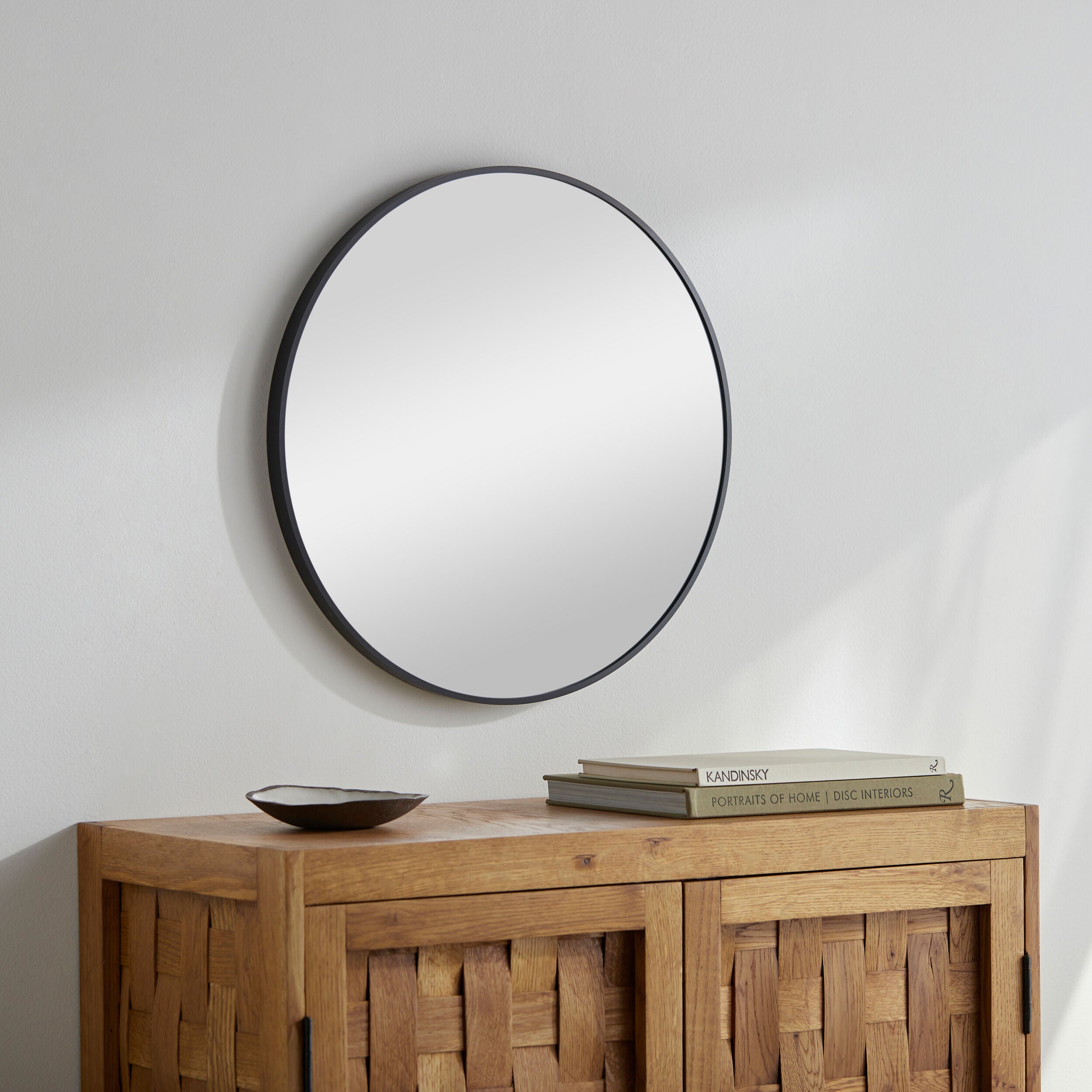 Round mirror with black frame on a white wall above a wooden console table.