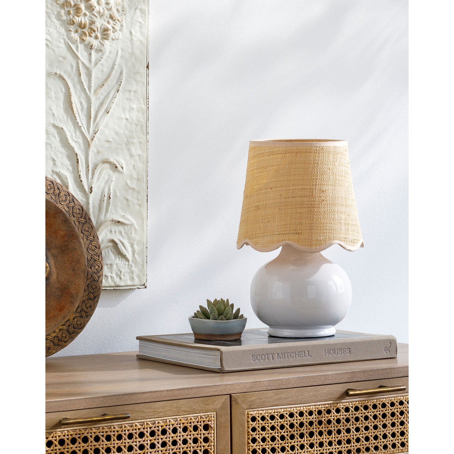 White lamp with a beige lampshade on a wooden surface with a decorative wall in the background