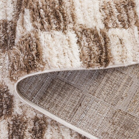 A shaggy area rug with a geometric pattern in ivory and brown tones.