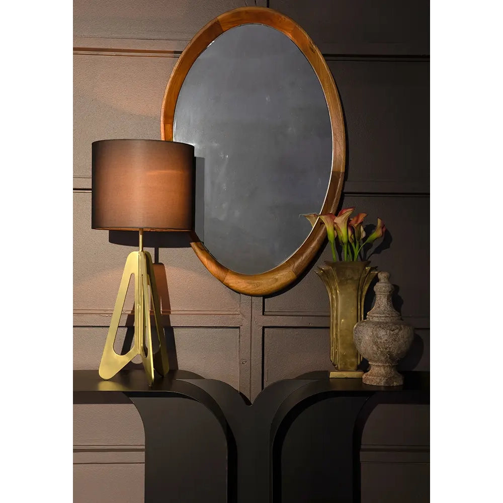Round wooden mirror on a wall with a lamp and decorative items below.