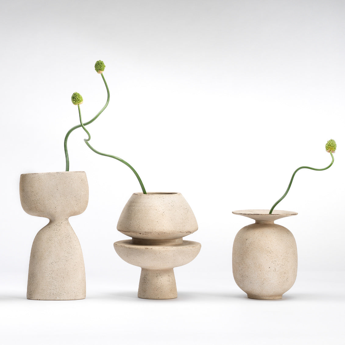 Three beige ceramic vases with plant stems on a white background
