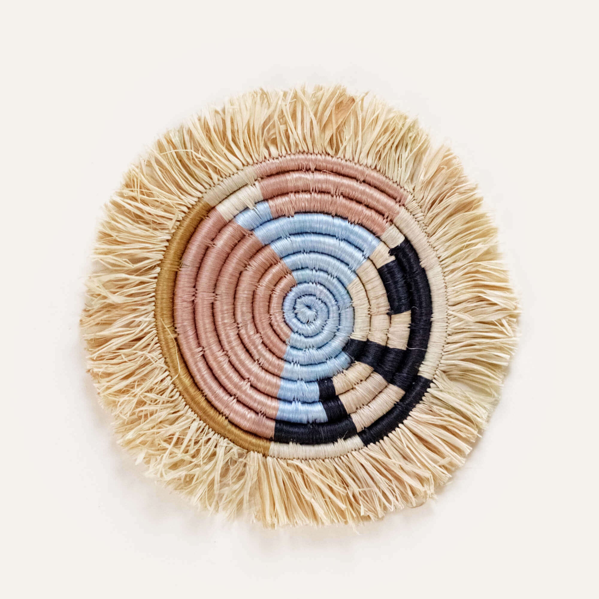 Round woven coaster with fringed edge and colorful spiral design on a white background