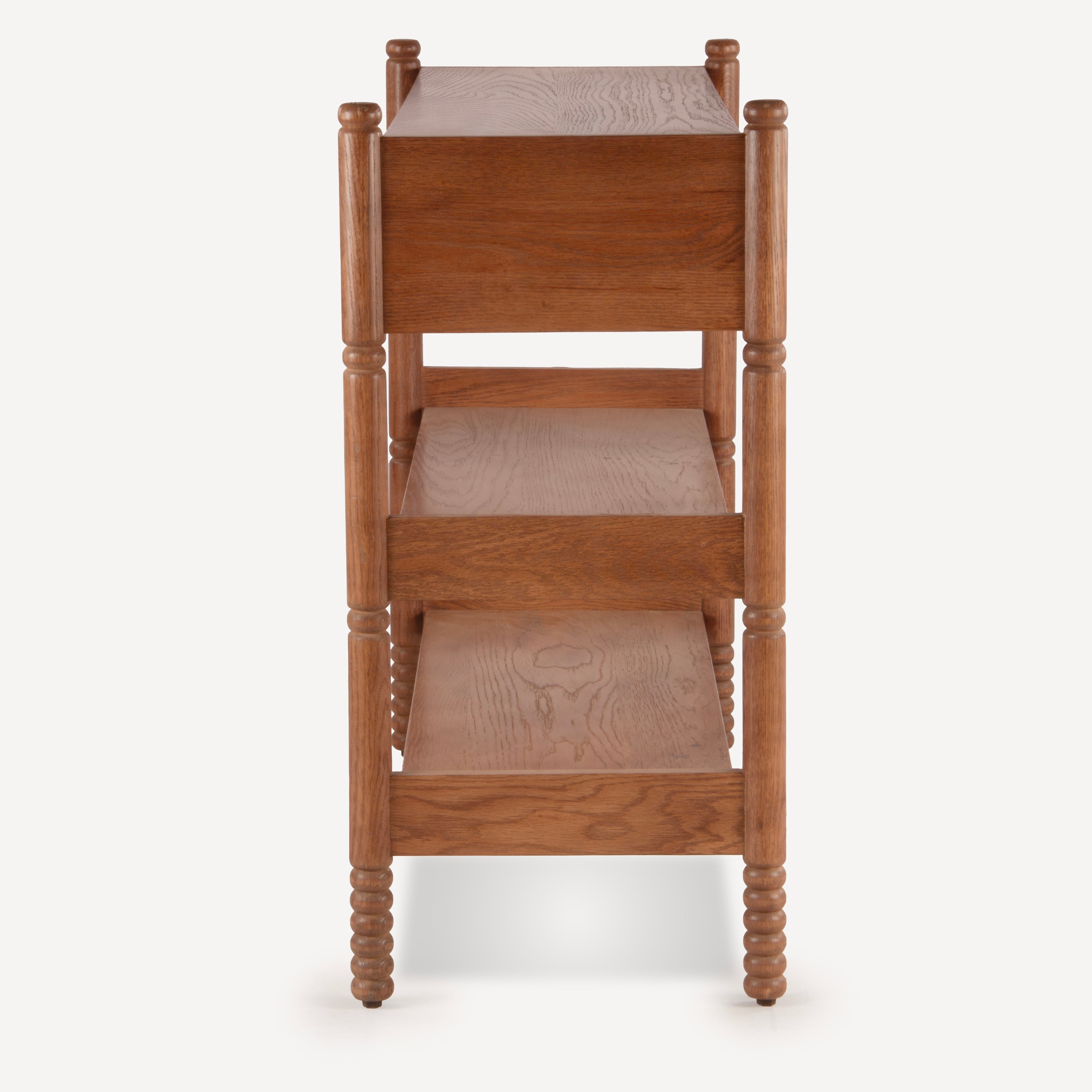 A three-tier wooden storage shelf with turned spindle legs, shown from the front against a light gray background.