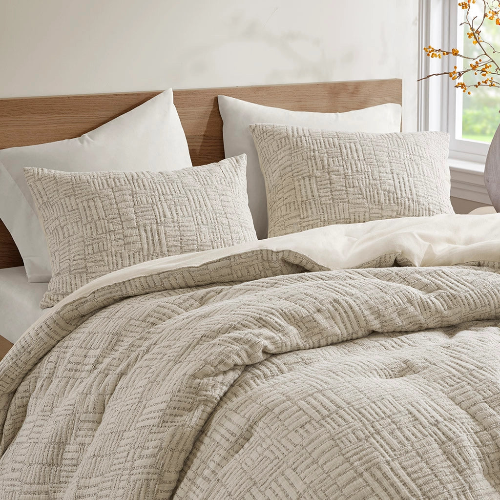 Neatly made bed with textured beige bedding and white pillows in a bright room.