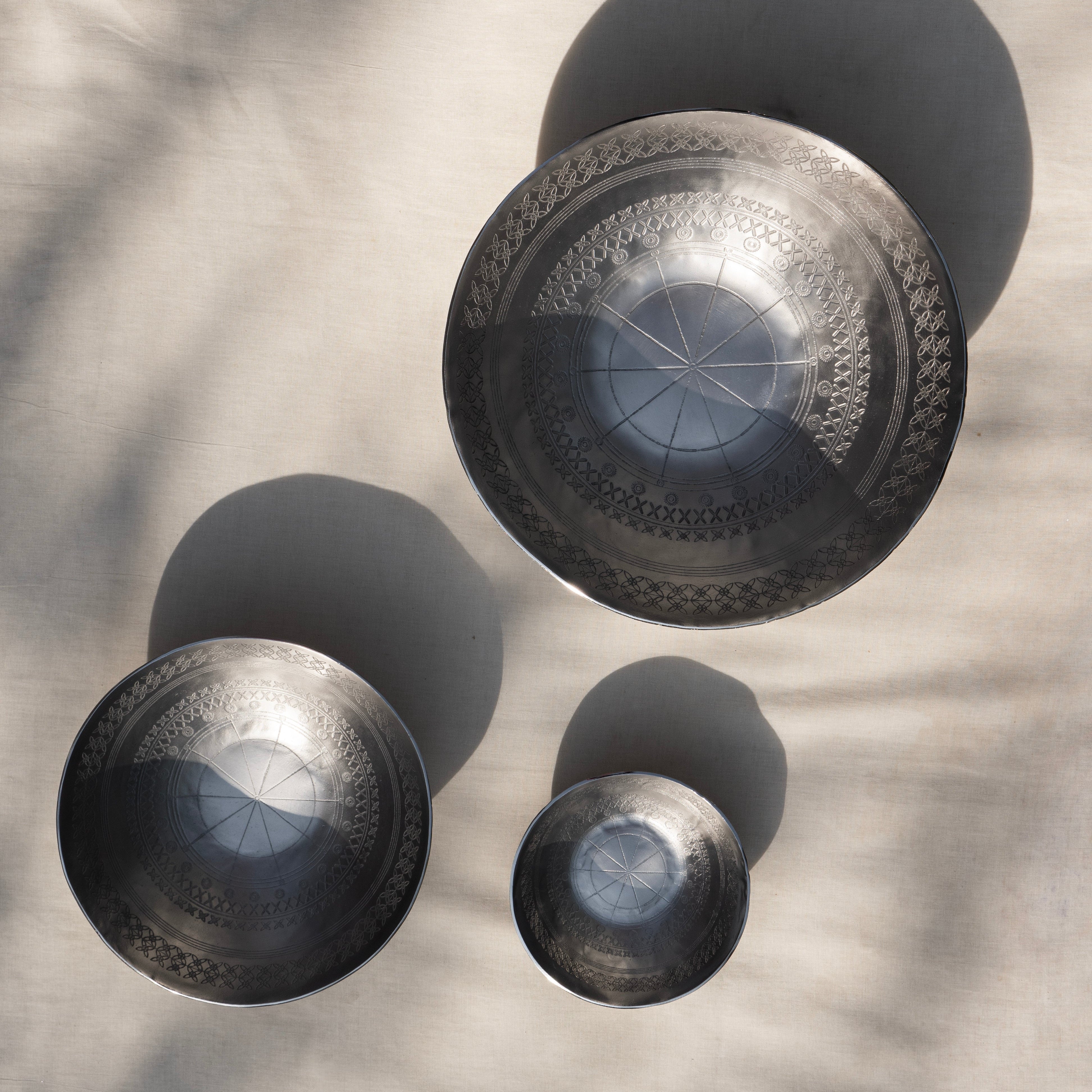 Set of three metallic bowls with intricate designs on a textured surface