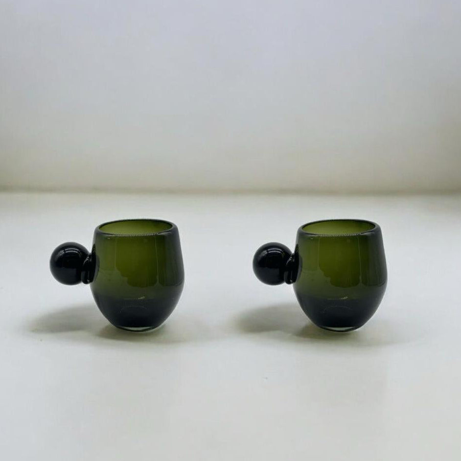 Two green glass cups with round handles on a white surface