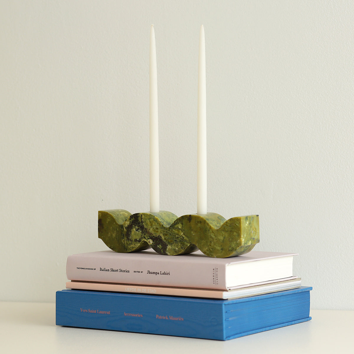 Green stone candle holder on top of books with two candles in the background