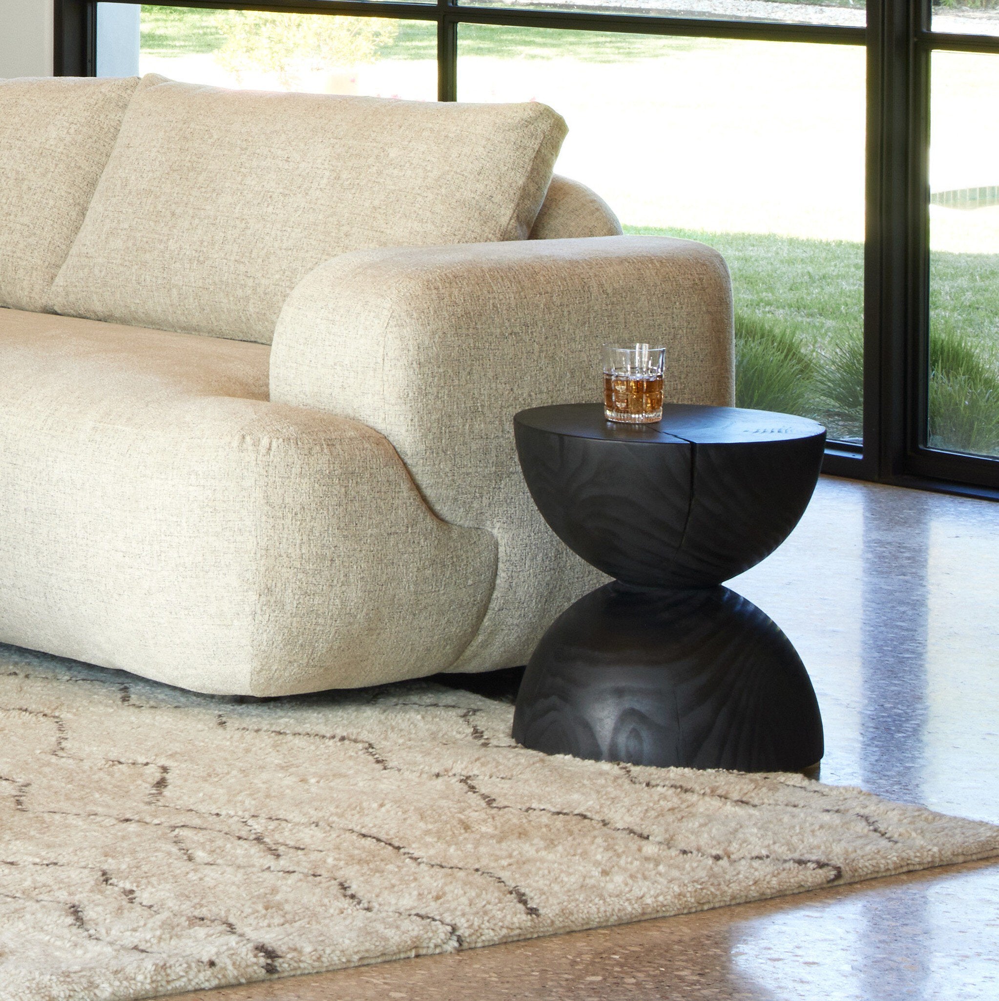 Beige sofa with a black side table and glass of whiskey in a modern living room.