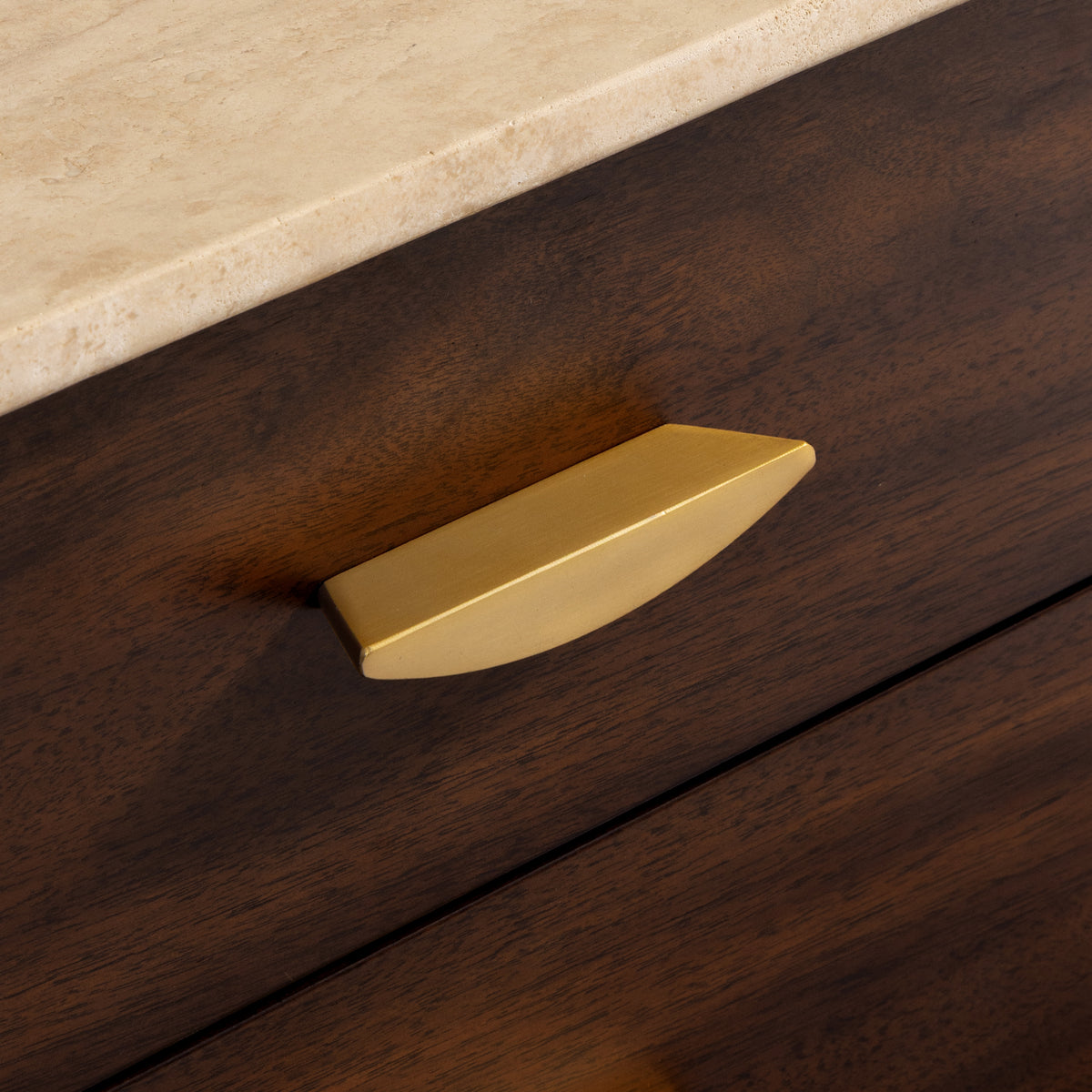 Gold cabinet handle on a wooden drawer with a beige countertop.