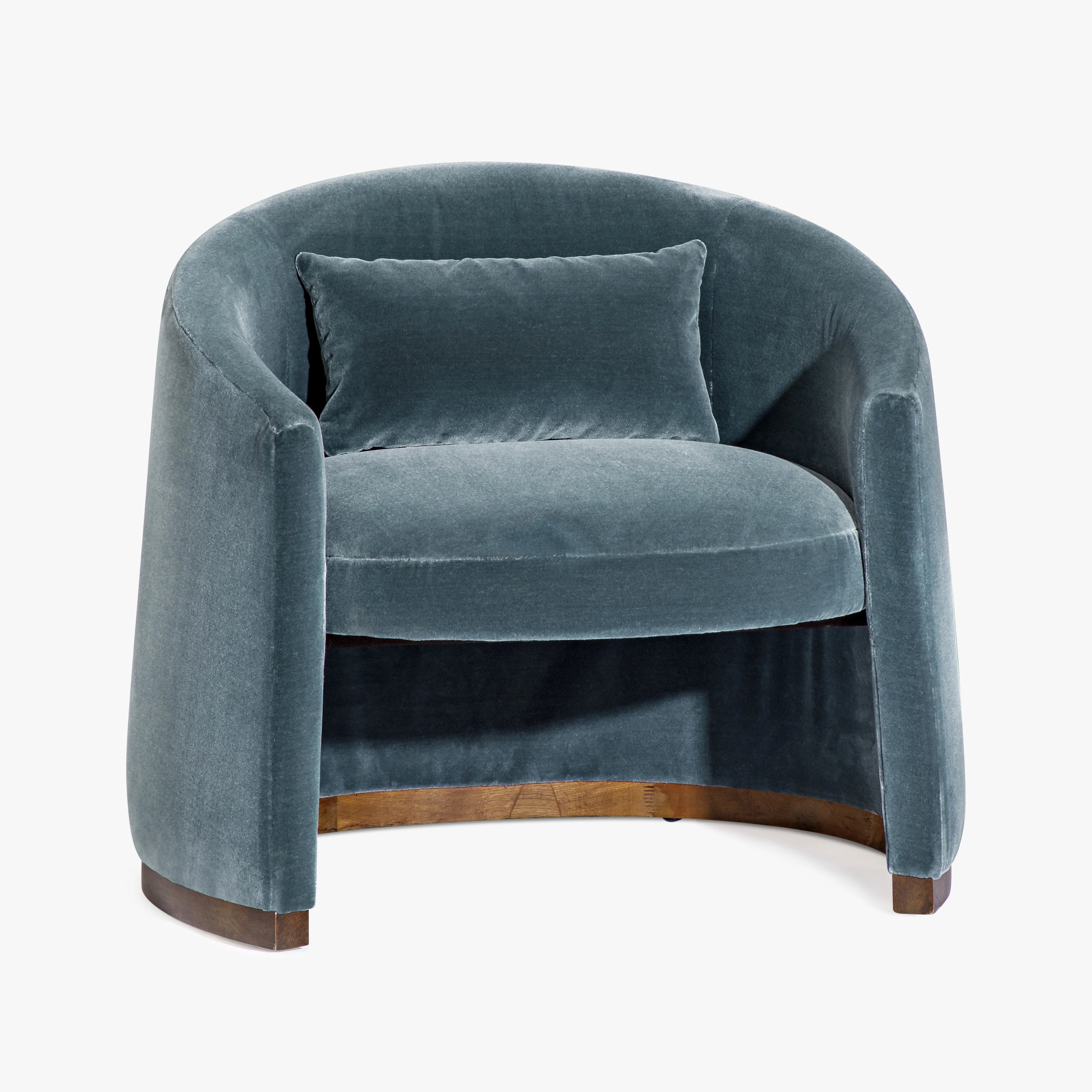 A modern barrel-style armchair upholstered in textured blue-gray velvet with a matching throw pillow, featuring a curved back, wooden base, and dark wood legs, shown against a plain white background.
