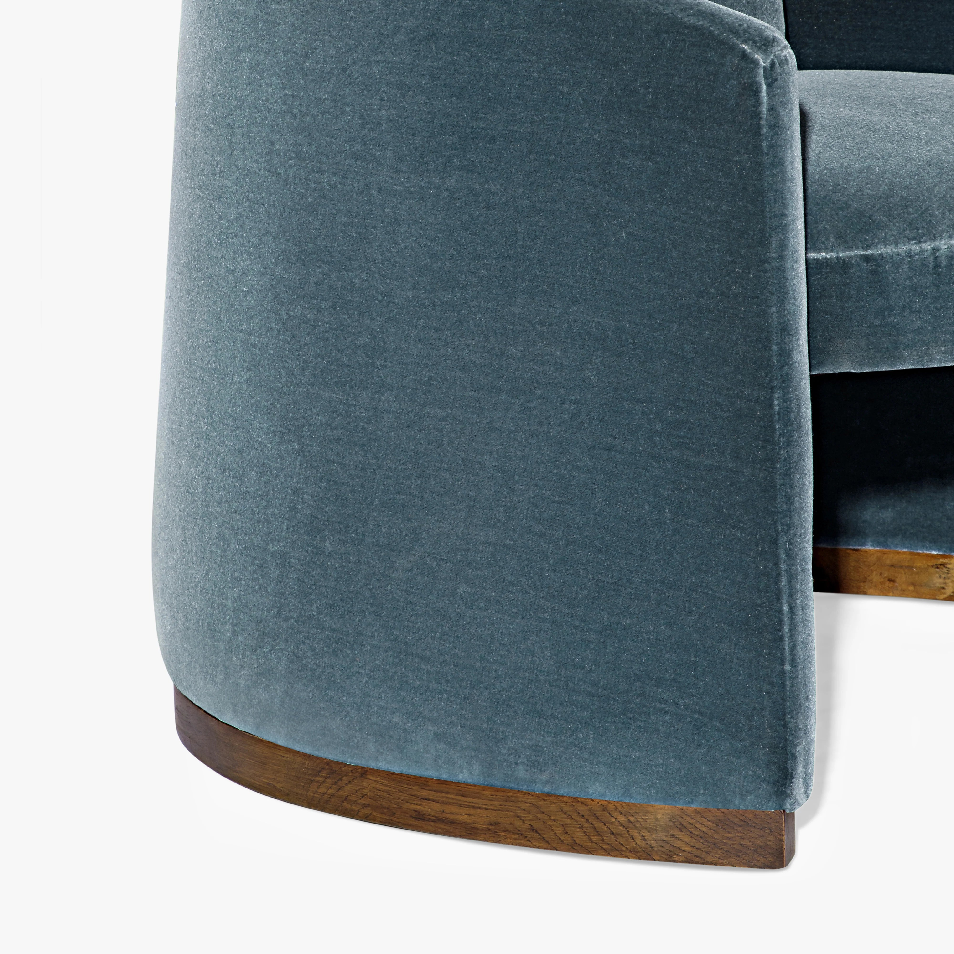 Close-up of a modern upholstered chair in textured blue-gray fabric with a curved wooden base trim, shown against a plain white background.