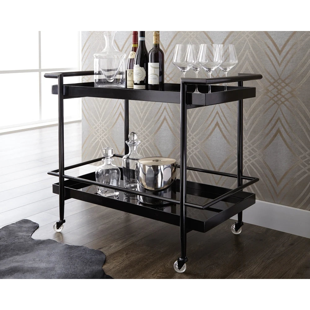 A black two-tier rolling bar cart with glass shelves, shown in a room setting with wine bottles, glasses, and barware on top and bottom shelves.