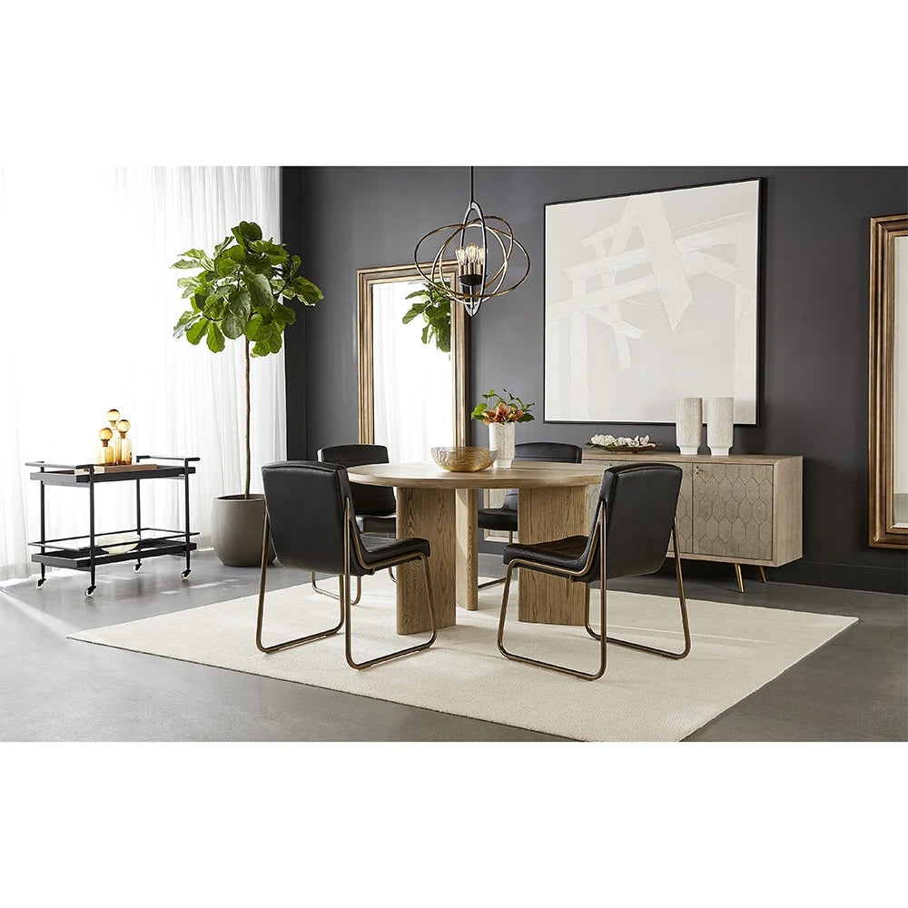 A modern dining room scene featuring a round light oak wood dining table surrounded by four black leather chairs with chrome legs, set on a cream area rug in a contemporary room with dark gray walls.
